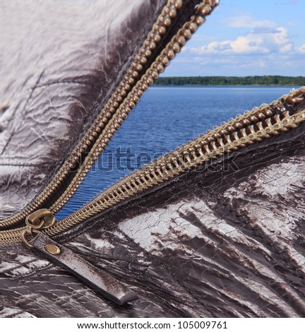 Zipper opened, sewn to a leather product, opens a window on a fine view of the dark blue sea, the river, the sky, clouds