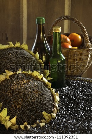 Crop of a seed of sunflower, sunflower oil in glass bottles and a wattled basket with tomatoes