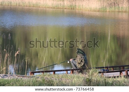 fisherman on river bank fishes in the early solar morning near a birchwood