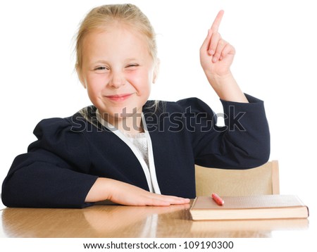 The schoolgirl is sitting at his desk and points a finger up on a white background.