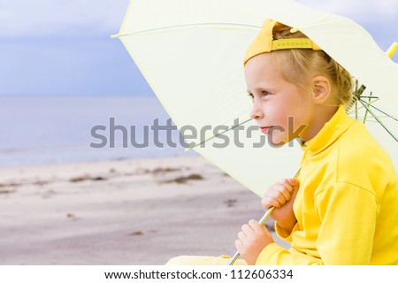The girl in yellow clothes with umbrella sitting on the beach.