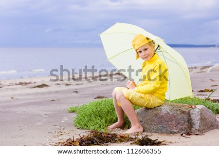 The girl in yellow clothes with umbrella sitting on the beach.