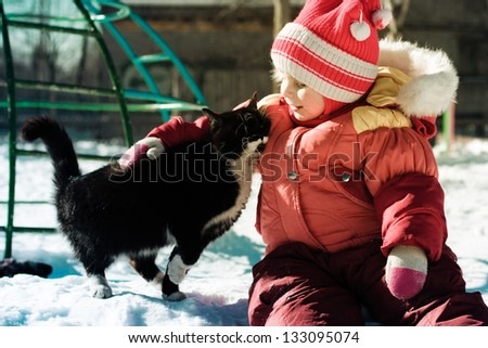 Funny happy child playing with cat outdoors in winter.