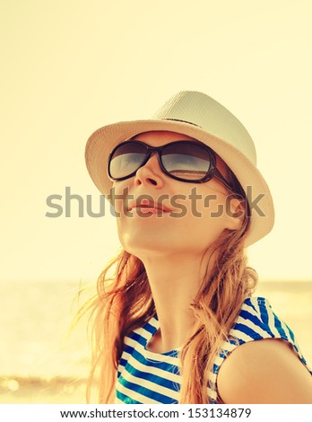 Relaxing beach woman enjoying the summer sun happy in a cap and sunglasses with face raised to the sunlight.