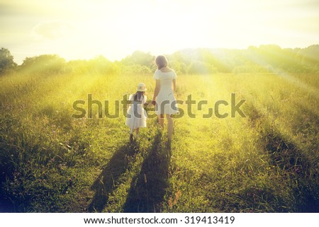 Mother and daughter walking on the sunny meadow.