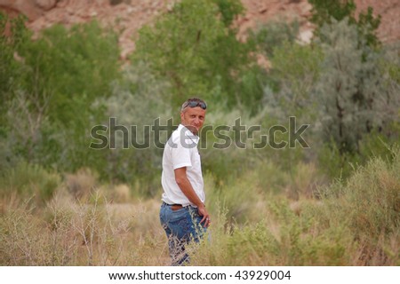 handsome white man with white shirt and blue jeans walking in the bush
