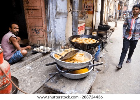Jaipur, India - 2014, December 31 : An Indian shop owner selling fried street food and a pedestrian walking in a street in Jaipur in Rajasthan, India