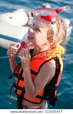 smiling little girl in life jacket and diving mask and snorkel on sea water background
