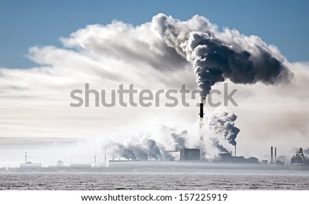 view of big factory with black smoke from its pipe on winter lake coast