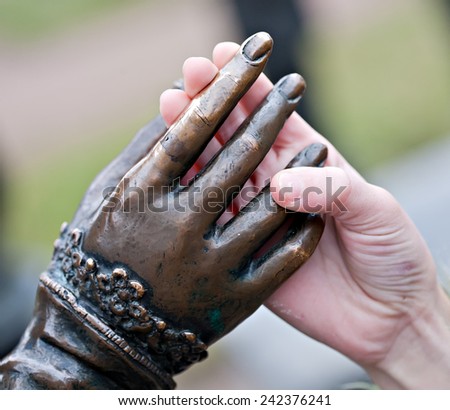 touch closeup of two hands: metal statue and human child