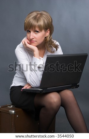 young business woman in white shirt and black skirt sitting on big suitcase with notebook on her knees