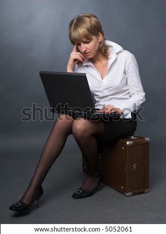 young business woman in white shirt and black skirt sitting on suitcase with notebook on her knees