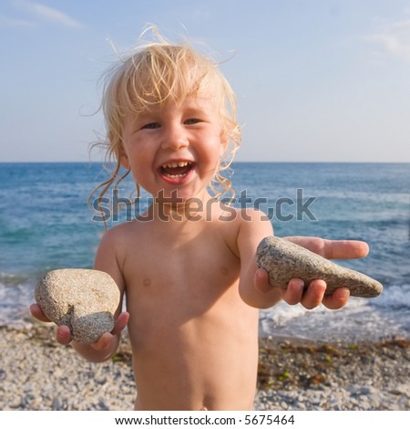 happy child on the pebble beach with two stones in hands