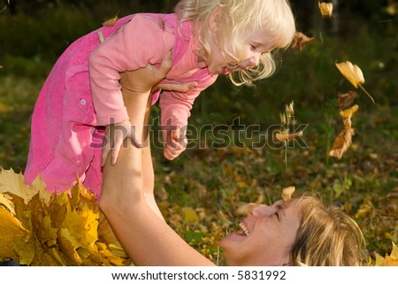 happy smiling woman with laughing little daughter in hands lying on the earth covered by yellow leaves