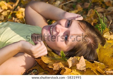 happy smiling woman lying on the earth covered by yellow maple leaves