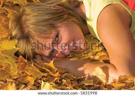 happy smiling woman lying on the earth covered by yellow maple leaves