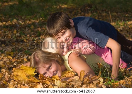 happy smiling woman with children lying on the earth covered by yellow leaves
