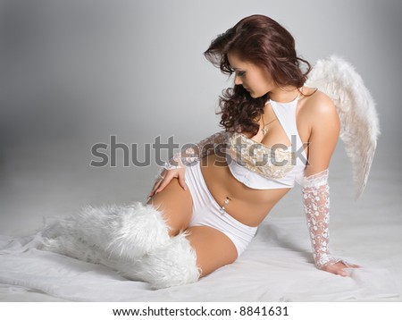 beautiful woman sadly sitting in white dress and angel wings on the back