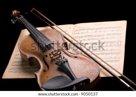 old violin with fiddlestick on music sheet isolated on black background