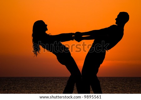 silhouettes of happy young couple holding by hands on orange sea sunset background