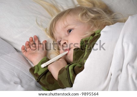 sick child in bed under blanket with thermometer in mouth