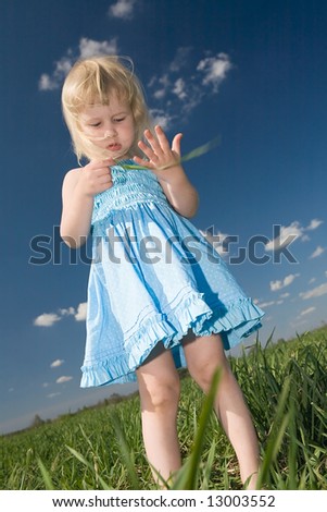little girl with blade of grass in hands on green summer meadow