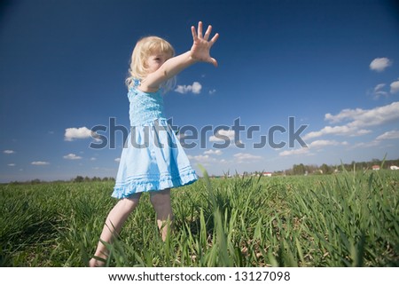 funny little girl in blue dress on green meadow and blue sky background
