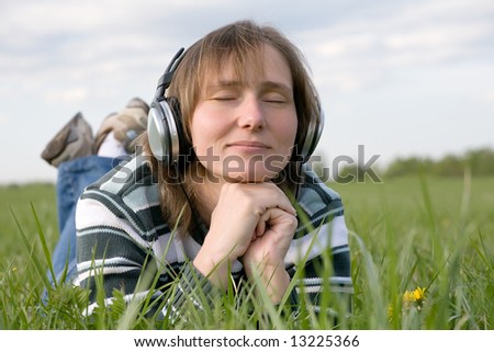 young woman in headphones listening to the music lying on green grass meadow