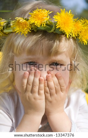 funny little girl in dandelion wreath hiding her face behind hands