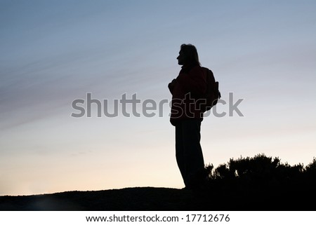 black silhouette of tourist woman in profile with rucksack on evening sky background