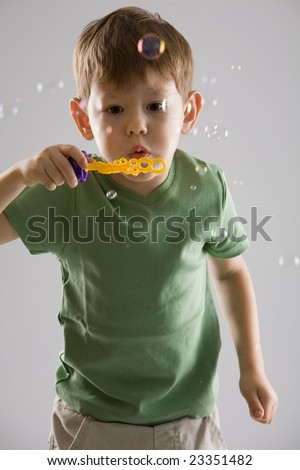 boy in a green T-shirt blows soap bubbles, on grey background