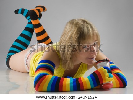funny girl in long multi-coloured socks and gloves lies on the floor and drinks through a straw