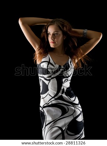 Beautiful girl in a white-black dress with flying hairs holds hands above head on black background
