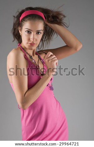 Beautiful girl in pink dress holds flying hairs in hand on grey background