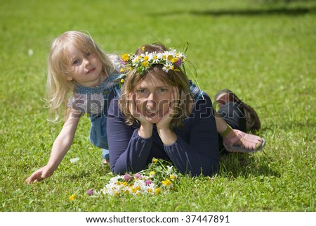 Mum and daughter lie on a green grass, the daughter gets on mum