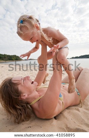 Mum with daughter play on beach, mum lies on sand and holds a daughter upward