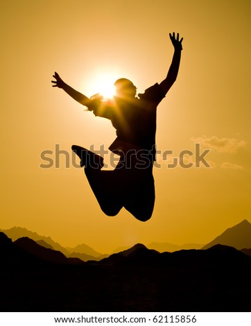 black silhouette of man in happy jump on orange sunset sky and desert mountain background