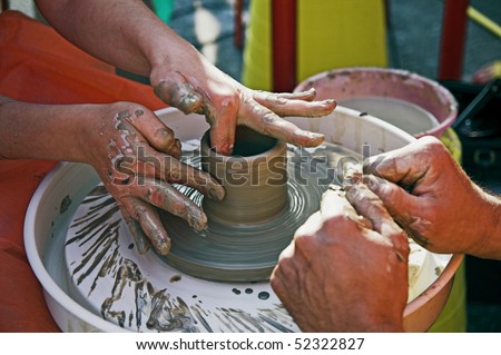 potter\'s hands guiding woman\'s hands to help her learn pottery
