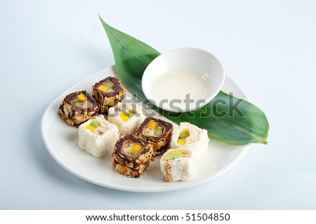 tasty Japanese sweet dessert. Rolls with various fruit. Pancake, chocolate cream, coconut and almonds outside. Served with coconut milk sauce on a leaf of spathifyllum on a white dish