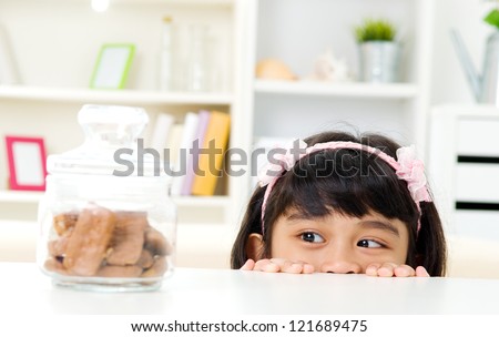 Asian girl peeking over table at cookies inside the glass bottle
