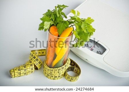 healthy vegetables in a glass surrounded by a measuring tape, bathroom scales in background