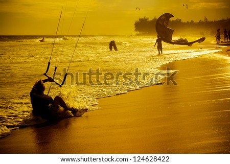 sand beach, people swimming and ride on kite on sunset.