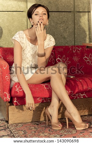 fashion portrait of young, slim, beautiful model in white dress sitting in on a sofa