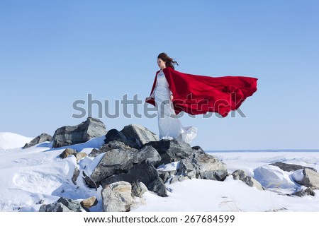 Young and beautiful bride with the red fabric playing with wind in winter background.