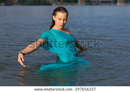Attractive girl have fun, dives and drowned at the urban beach in the water. Woman portrait with blue dress.