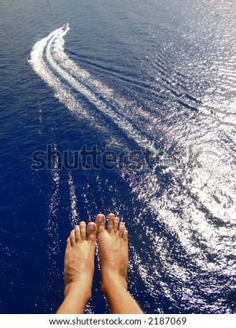 man parasailing over ocean with feet and boat in view