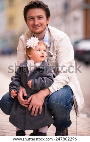 Father hugs his daughter on the street. A little one year old girl stands back to her father. A young man smile to the camera