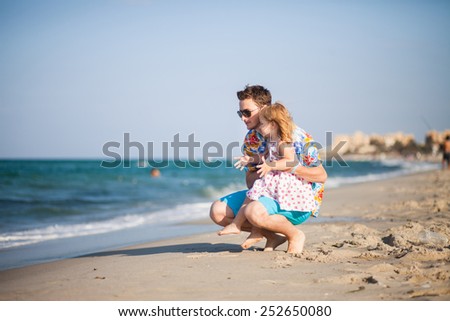 Father and daughter on the beach near the sea. Young man hugs little baby girl. It is emotional scene of relations between child and parent