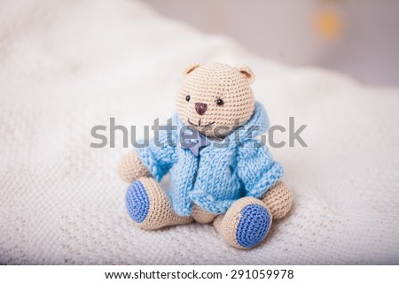 beige crocheted bear dressed on blue sweater on light background