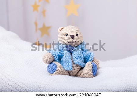 beige crocheted bear dressed on blue sweater on light background